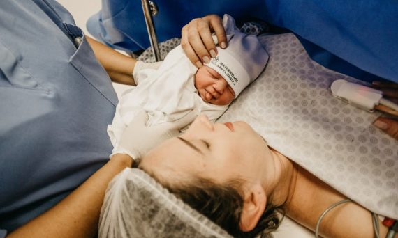 A mother cradling her newborn immediately after childbirth in a hospital setting.