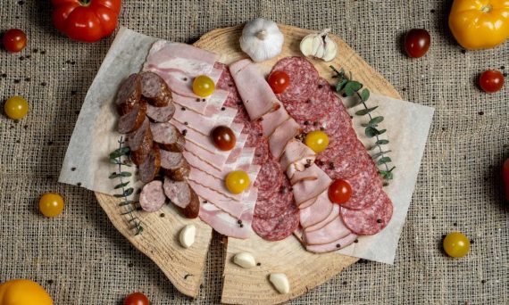 A high-angle view of assorted cured meats and fresh tomatoes on a rustic wooden board.