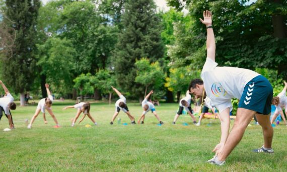 Kids stretching exercises in a park guided by a coach, promoting fitness and fun.
